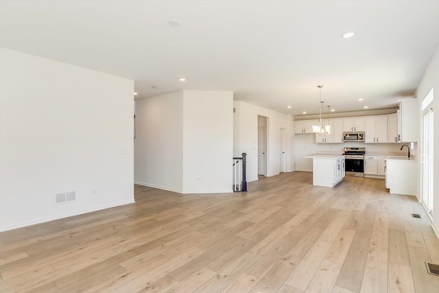 unfurnished living room featuring recessed lighting, a sink, visible vents, light wood-type flooring, and an inviting chandelier