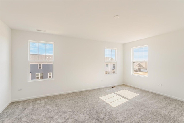 unfurnished room featuring a healthy amount of sunlight, carpet, visible vents, and baseboards