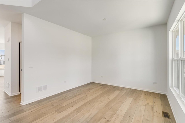 empty room featuring light wood finished floors, baseboards, and visible vents