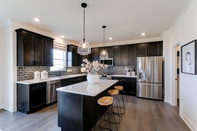 kitchen featuring stainless steel appliances, crown molding, wood-type flooring, decorative light fixtures, and a kitchen island