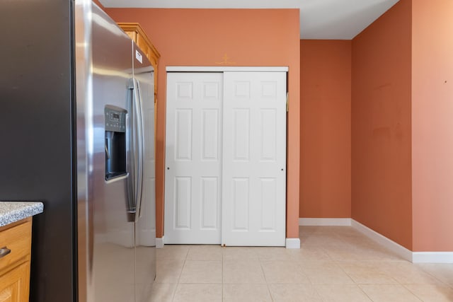 interior space with a closet, baseboards, stainless steel fridge, and light tile patterned flooring