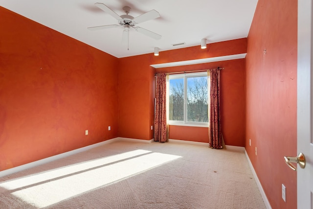 carpeted spare room with visible vents, baseboards, and ceiling fan