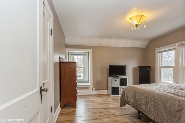 bedroom featuring multiple windows, light hardwood / wood-style flooring, lofted ceiling, and an inviting chandelier