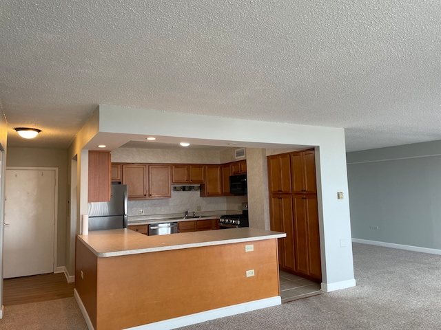 kitchen with sink, stainless steel appliances, light carpet, a textured ceiling, and decorative backsplash