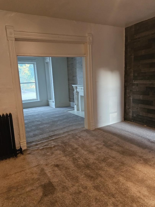 carpeted spare room with a large fireplace and radiator heating unit