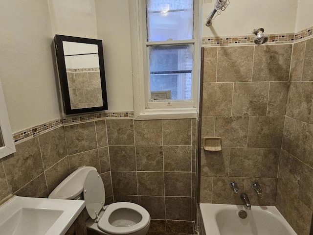 full bathroom with sink, tiled shower / bath combo, toilet, and tile walls