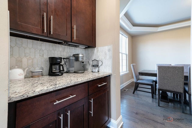 kitchen with tasteful backsplash, dark wood-type flooring, baseboards, dark brown cabinetry, and a raised ceiling