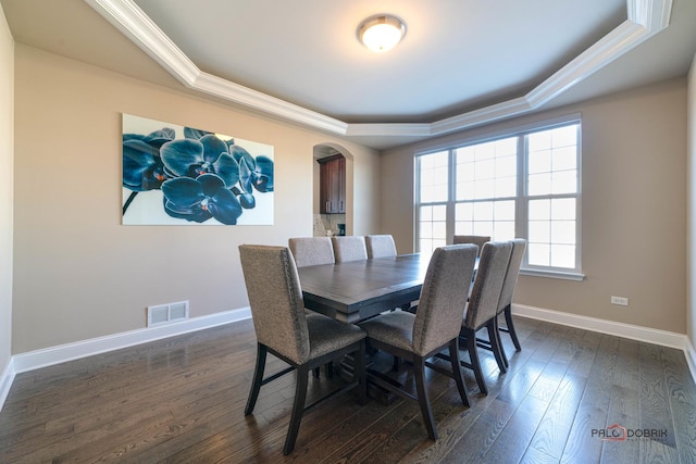 dining space featuring dark wood-style floors, visible vents, baseboards, arched walkways, and a raised ceiling