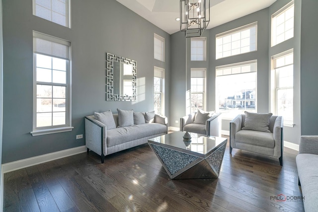 living area with dark wood-style floors, baseboards, a towering ceiling, and a healthy amount of sunlight