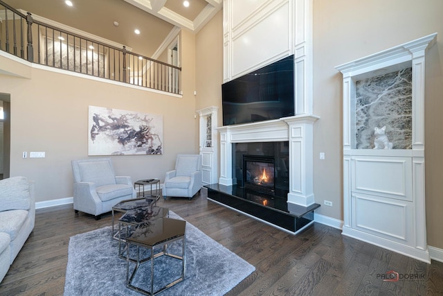 living area with baseboards, dark wood-type flooring, a high ceiling, and a glass covered fireplace