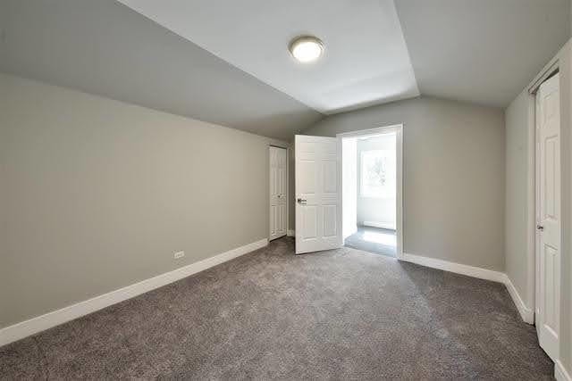 unfurnished bedroom with dark colored carpet and vaulted ceiling