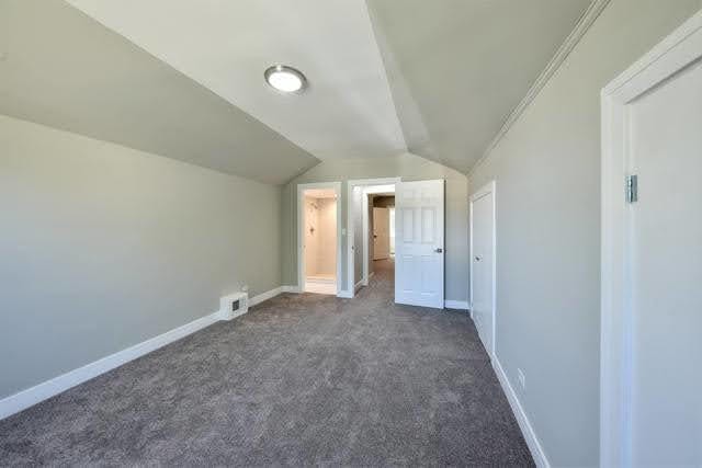 bonus room with dark colored carpet and lofted ceiling