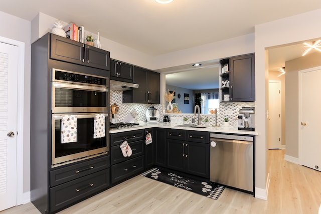 kitchen with tasteful backsplash, sink, stainless steel appliances, and light hardwood / wood-style floors