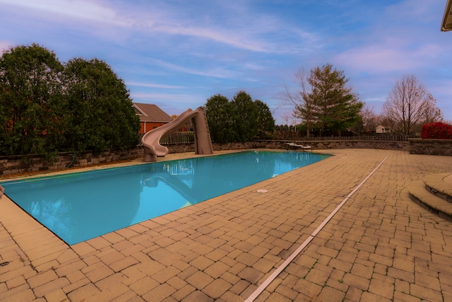 pool at dusk with a patio area and a water slide