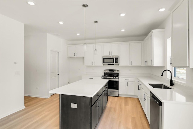 kitchen featuring decorative light fixtures, light countertops, appliances with stainless steel finishes, a kitchen island, and a sink