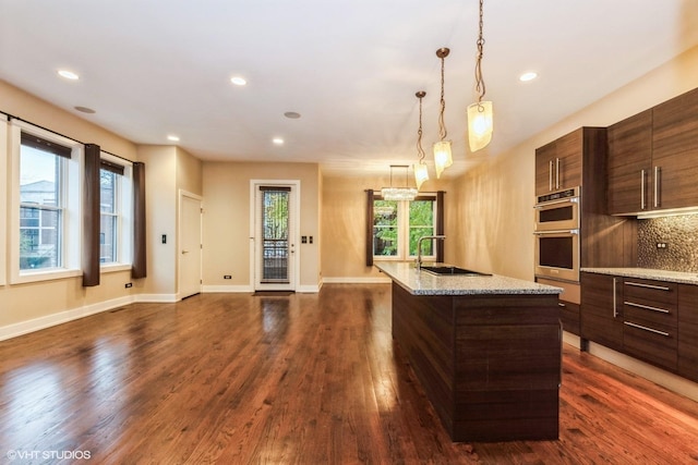 kitchen with double oven, a kitchen island with sink, sink, and plenty of natural light