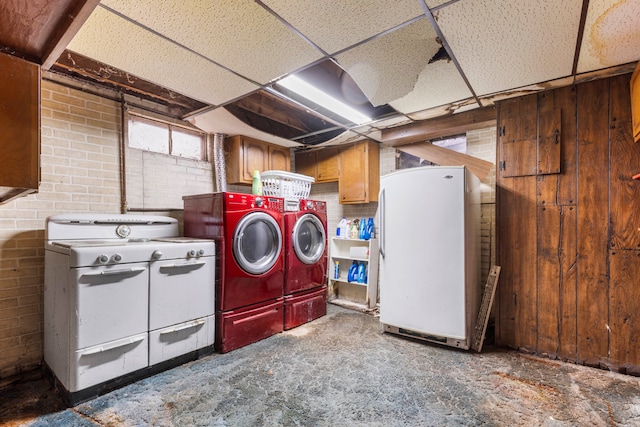 washroom with washing machine and dryer, wooden walls, cabinets, and brick wall