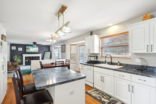 kitchen with white dishwasher, sink, ceiling fan, white cabinetry, and a tiled fireplace