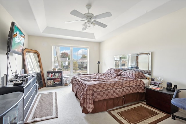 carpeted bedroom with a raised ceiling and ceiling fan