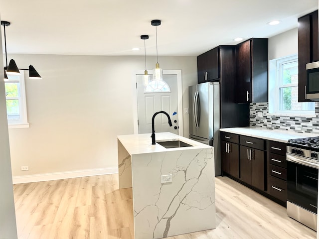 kitchen featuring sink, pendant lighting, an island with sink, light hardwood / wood-style floors, and stainless steel range with gas stovetop