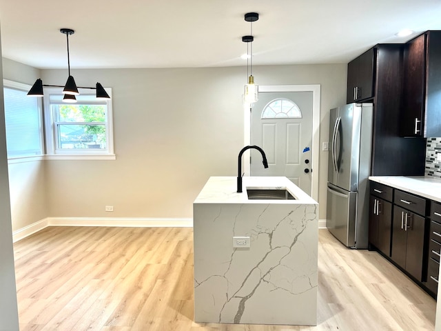 kitchen with stainless steel fridge, an island with sink, decorative light fixtures, and sink