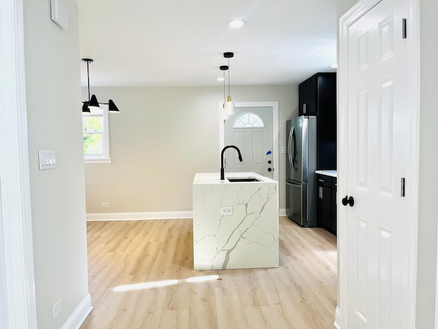 kitchen featuring stainless steel fridge, light wood-type flooring, hanging light fixtures, and sink