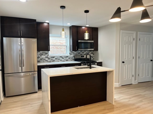 kitchen with light wood-type flooring, stainless steel appliances, a center island with sink, and sink