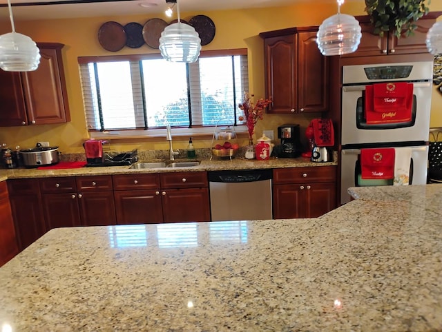 kitchen featuring light stone counters, sink, hanging light fixtures, and appliances with stainless steel finishes