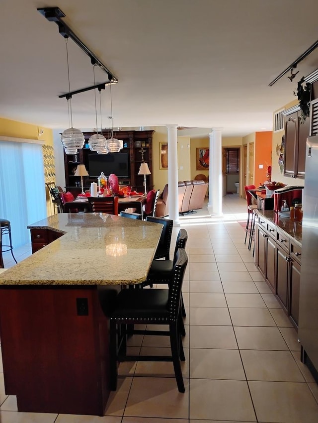 kitchen with light stone countertops, a kitchen breakfast bar, ornate columns, pendant lighting, and a large island