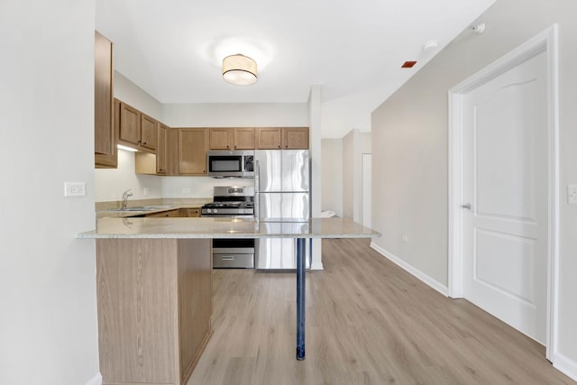 kitchen featuring sink, a breakfast bar area, kitchen peninsula, stainless steel appliances, and light hardwood / wood-style floors