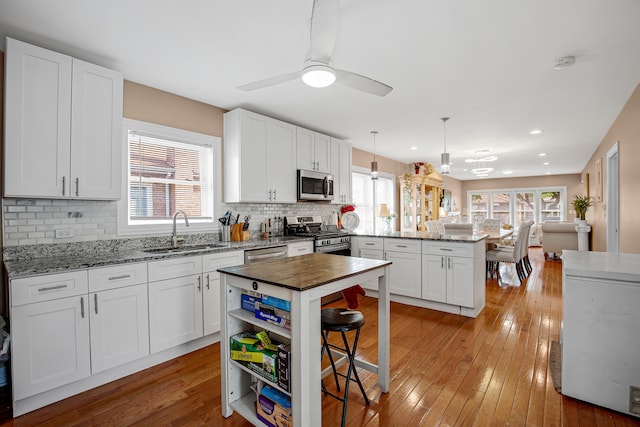 kitchen featuring sink, hanging light fixtures, light hardwood / wood-style floors, white cabinetry, and stainless steel appliances