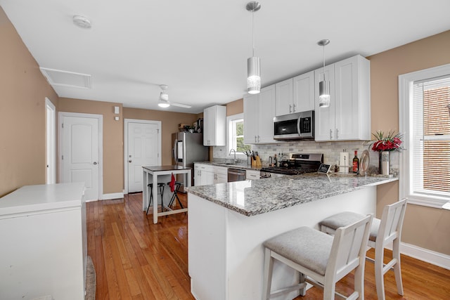 kitchen featuring kitchen peninsula, a kitchen bar, light wood-type flooring, stainless steel appliances, and white cabinets