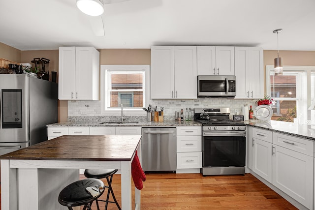 kitchen featuring sink, stainless steel appliances, light hardwood / wood-style flooring, pendant lighting, and white cabinets