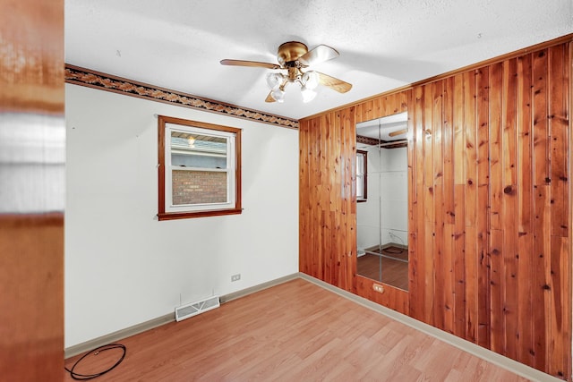 unfurnished bedroom featuring hardwood / wood-style flooring, ceiling fan, wood walls, and a closet