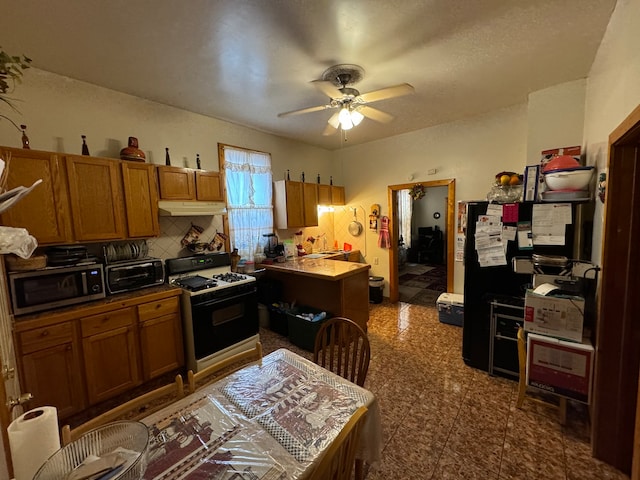 kitchen with ceiling fan, black refrigerator, decorative backsplash, and white range with gas stovetop