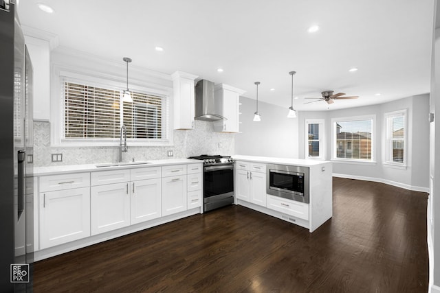 kitchen with sink, stainless steel appliances, wall chimney range hood, kitchen peninsula, and pendant lighting