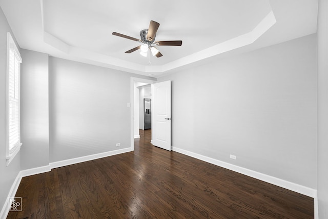 empty room with a raised ceiling, ceiling fan, and dark wood-type flooring