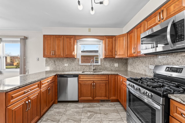 kitchen featuring light stone countertops, decorative backsplash, kitchen peninsula, stainless steel appliances, and sink