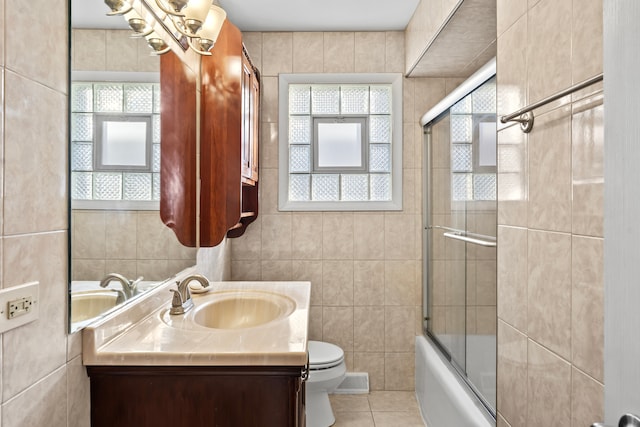 full bathroom with tile patterned flooring, enclosed tub / shower combo, toilet, vanity, and tile walls