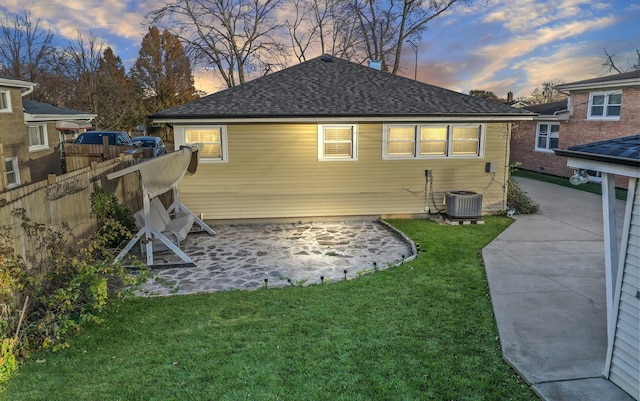 back house at dusk featuring a lawn, a patio area, and central AC unit