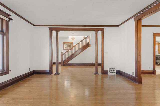 empty room featuring a chandelier, light hardwood / wood-style floors, a wealth of natural light, and decorative columns