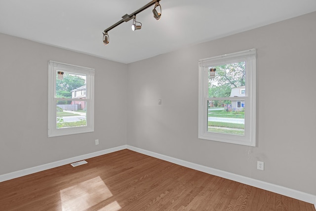 empty room featuring wood-type flooring, track lighting, and a wealth of natural light