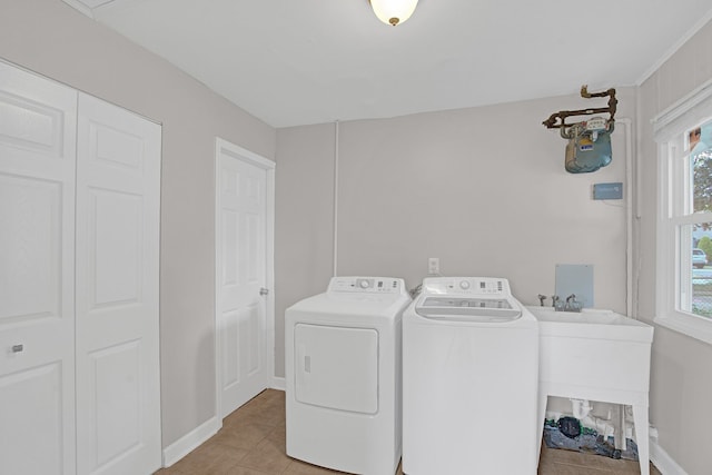 clothes washing area with washing machine and dryer, plenty of natural light, light tile patterned floors, and sink