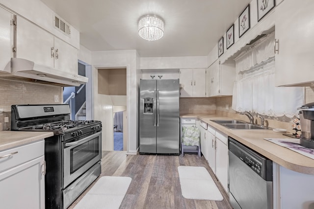 kitchen with hardwood / wood-style floors, backsplash, white cabinets, sink, and appliances with stainless steel finishes