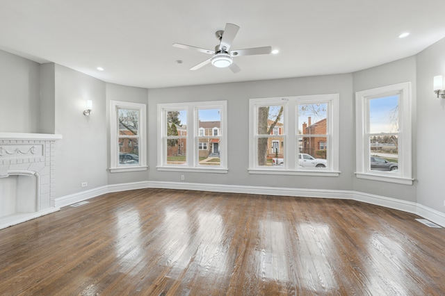 unfurnished living room with plenty of natural light, ceiling fan, dark hardwood / wood-style flooring, and a brick fireplace