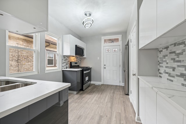 kitchen with white cabinetry, stainless steel appliances, light stone counters, light hardwood / wood-style flooring, and backsplash