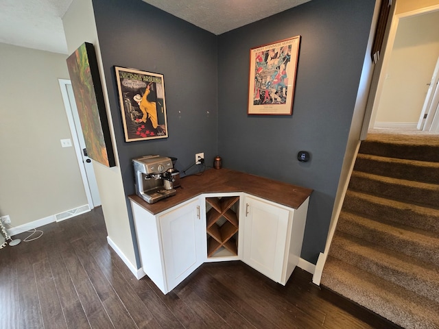 bar featuring white cabinets, dark wood-type flooring, and a textured ceiling