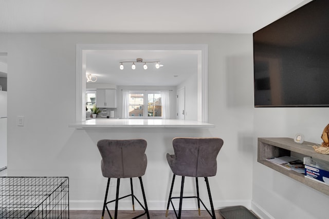 kitchen with kitchen peninsula, a breakfast bar, white fridge, white cabinets, and dark hardwood / wood-style floors