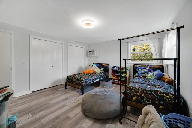 bedroom featuring a wall unit AC, light hardwood / wood-style flooring, and two closets