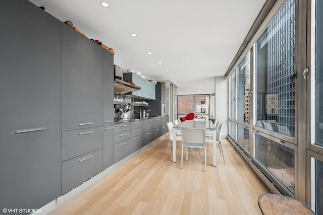 kitchen featuring tasteful backsplash, wall chimney exhaust hood, a breakfast bar, a baseboard heating unit, and light hardwood / wood-style floors